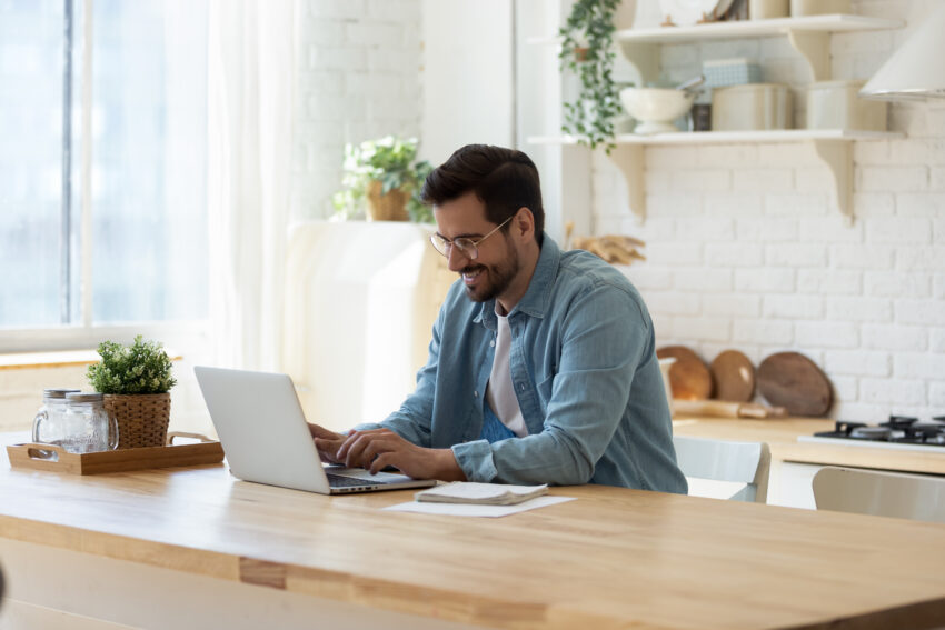 Smiling,Young,Man,Working,On,Laptop,In,Modern,Kitchen,,Checking